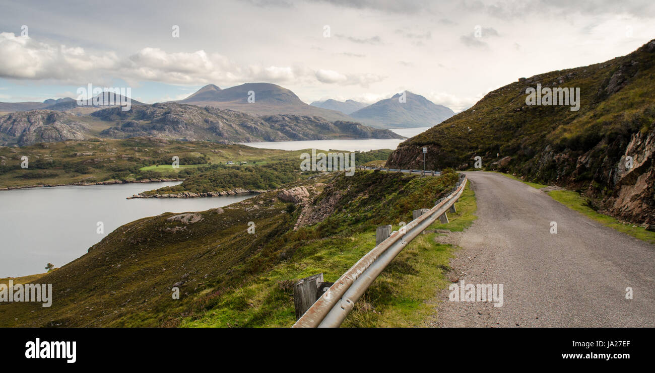 A narrow country road runs alongside the coast of Loch Torridon sea inlet on the Applecross Peninsula, with the mountains of the Torridon Hills rising Stock Photo