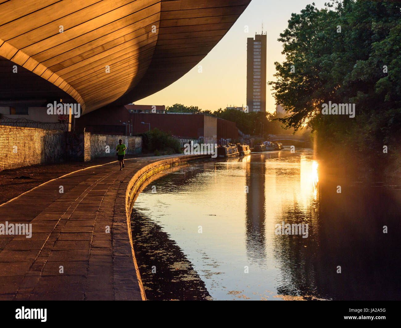 London, England - July 19, 2016: The Trellick Tower housing block and Westway road flyover are reflected in the waters of the Grand Union Canal at sun Stock Photo