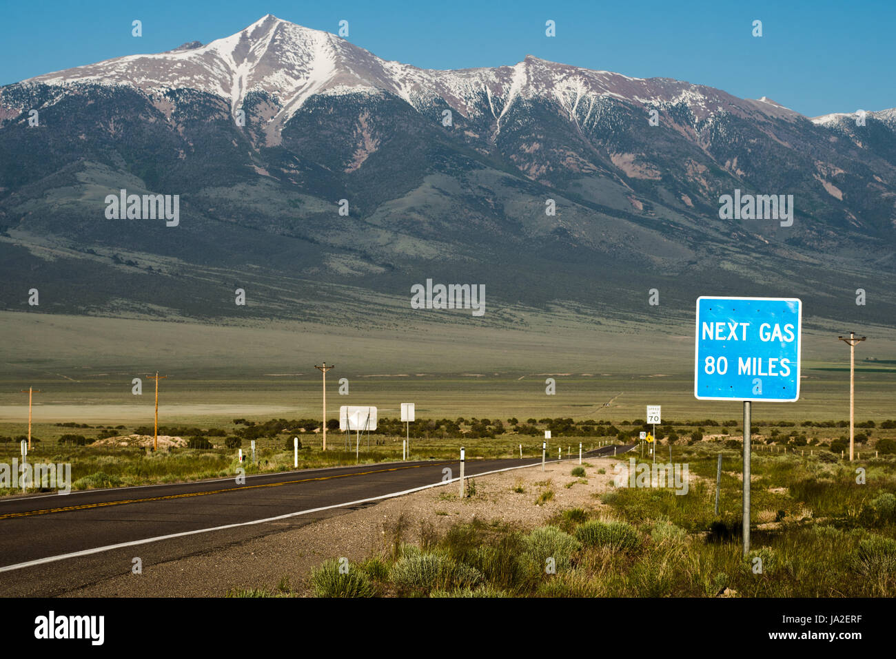 A sign warns that the next gas station is 80 miles away, with a snow-capped mountain in the background. White Pine County in Nevada. Stock Photo