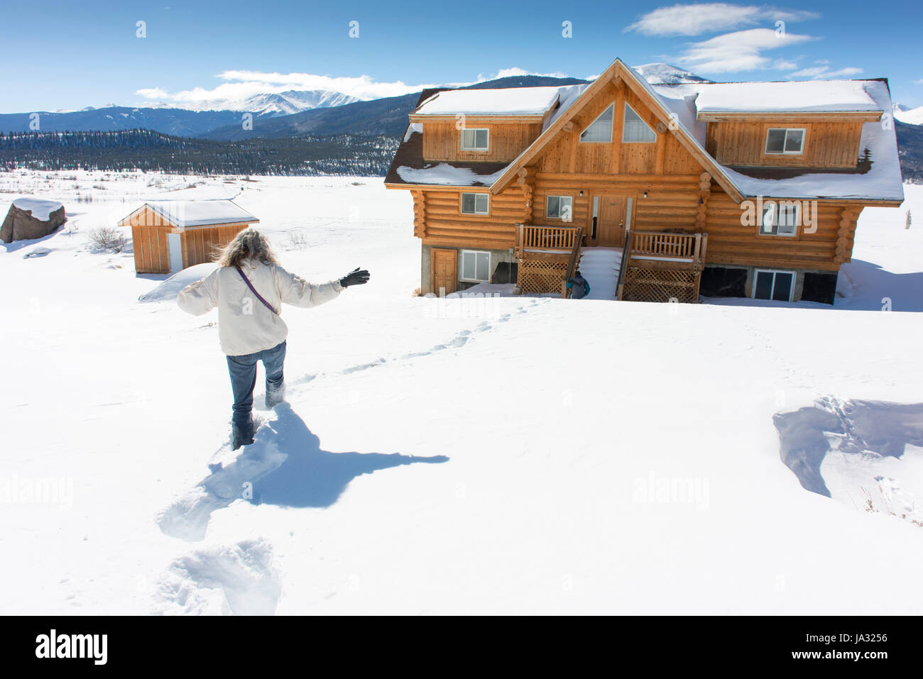 Woman walks through deep snow to get to log house. Stock Photo