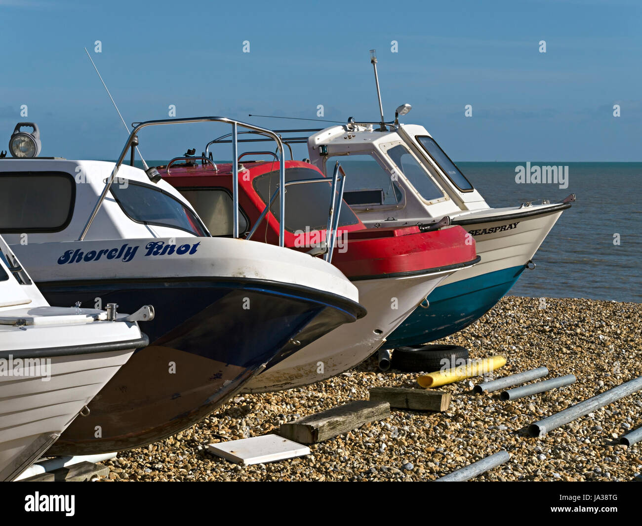 Row of four, small, sunlit boats beached on Eastbourne shingle with blue sky above, Eastbourne, East Sussex, England, UK Stock Photo