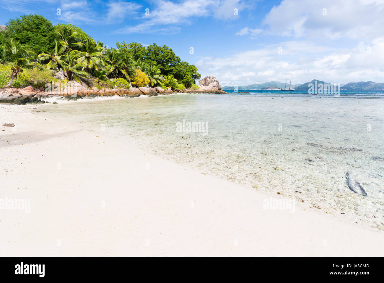 Calm water at Anse Severe in La Digue, Seychelles with palm trees and granite rocks in the background Stock Photo