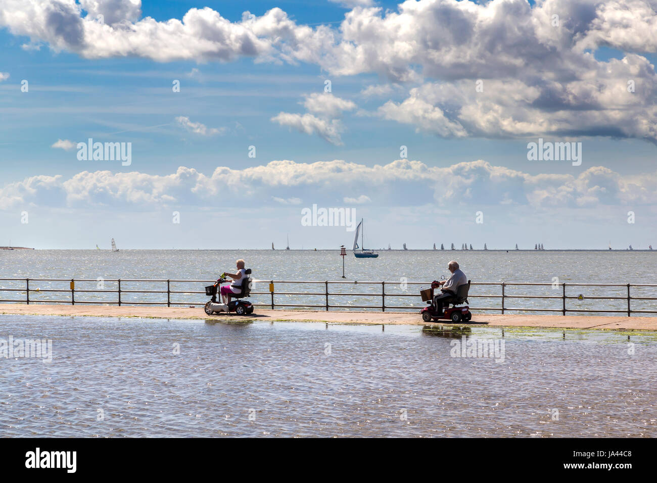 AND ELDERLY COUPLE USE THEIR MOBILITY SCOOTERS TO WALK THE DOG ALONG THE SEAFRONT AT BRIGHTLINGSEA IN ESSEX Stock Photo