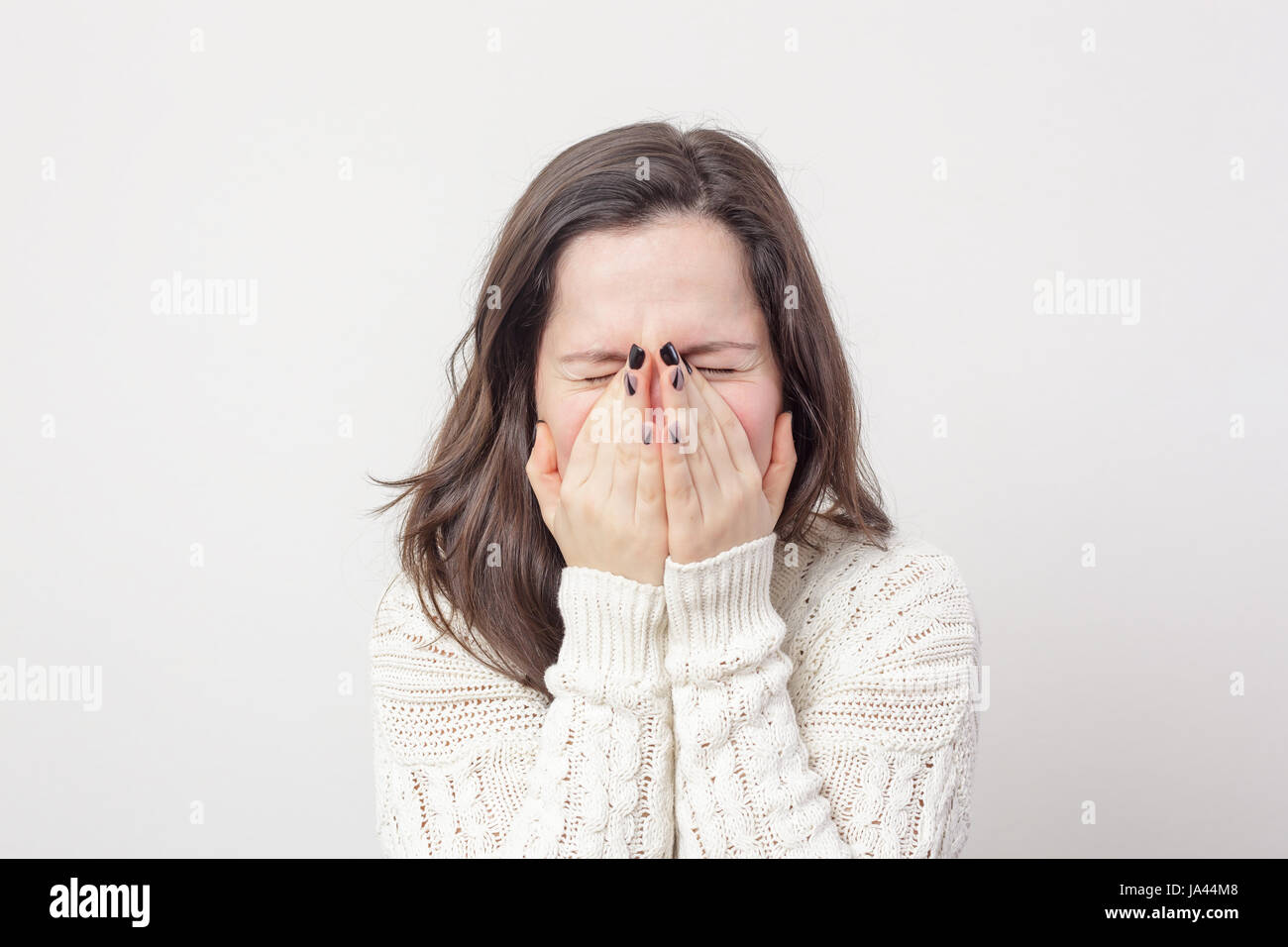 Girl sneezes, covering her face with with hands. To be afraid of something and turn a blind eye Stock Photo