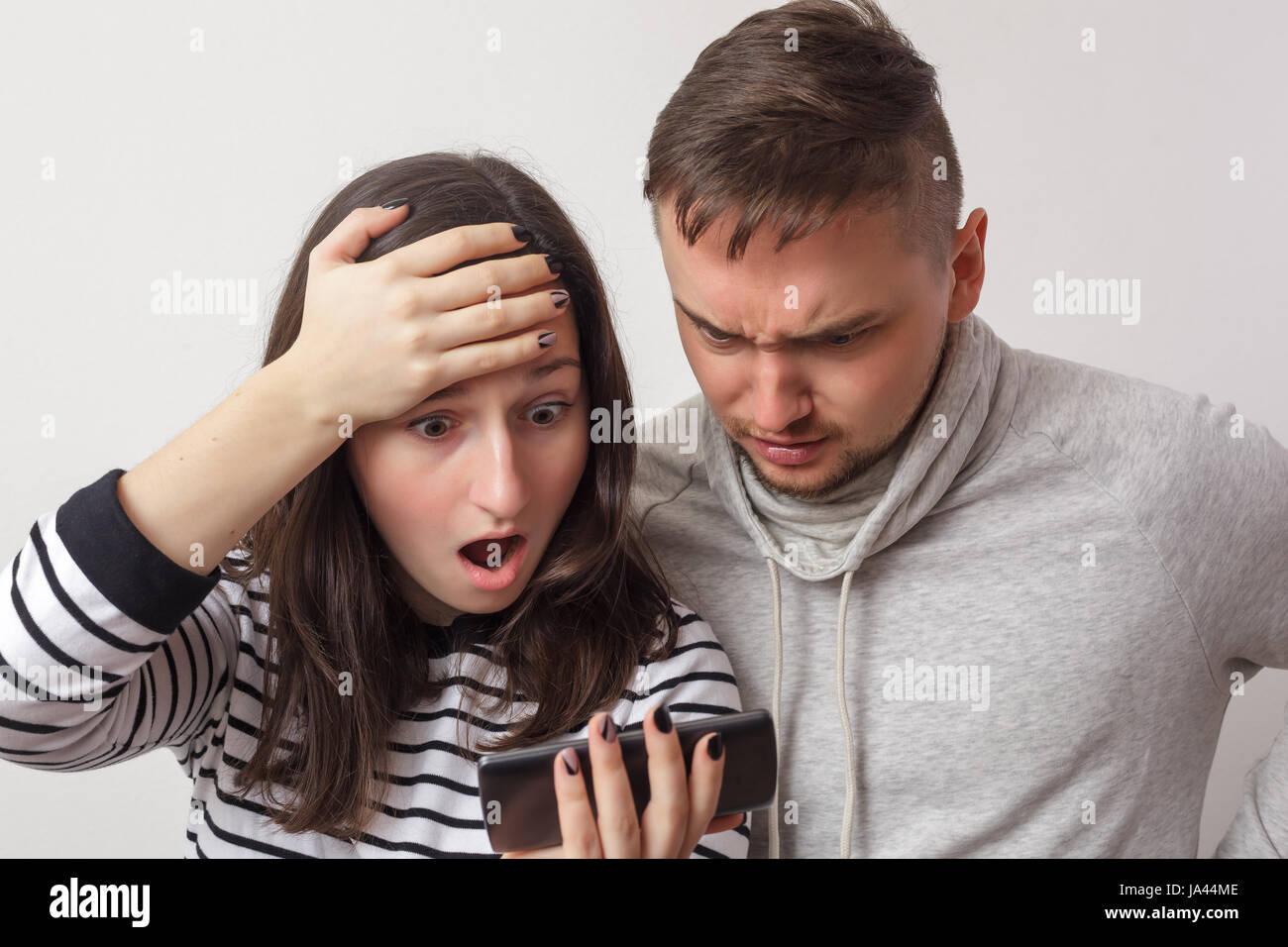 Couple of young people look at smartphone screen and see something frightening. Worry about what is happening Stock Photo