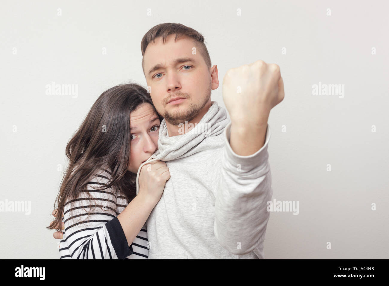 Brave young man protecting his girlfriend. He put his fist forward. She hides in fear behind him Stock Photo