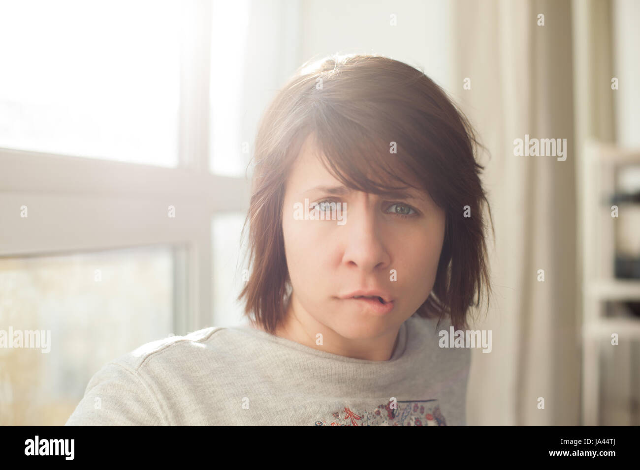 Caucasian woman in turmoil biting lips and frowns Stock Photo