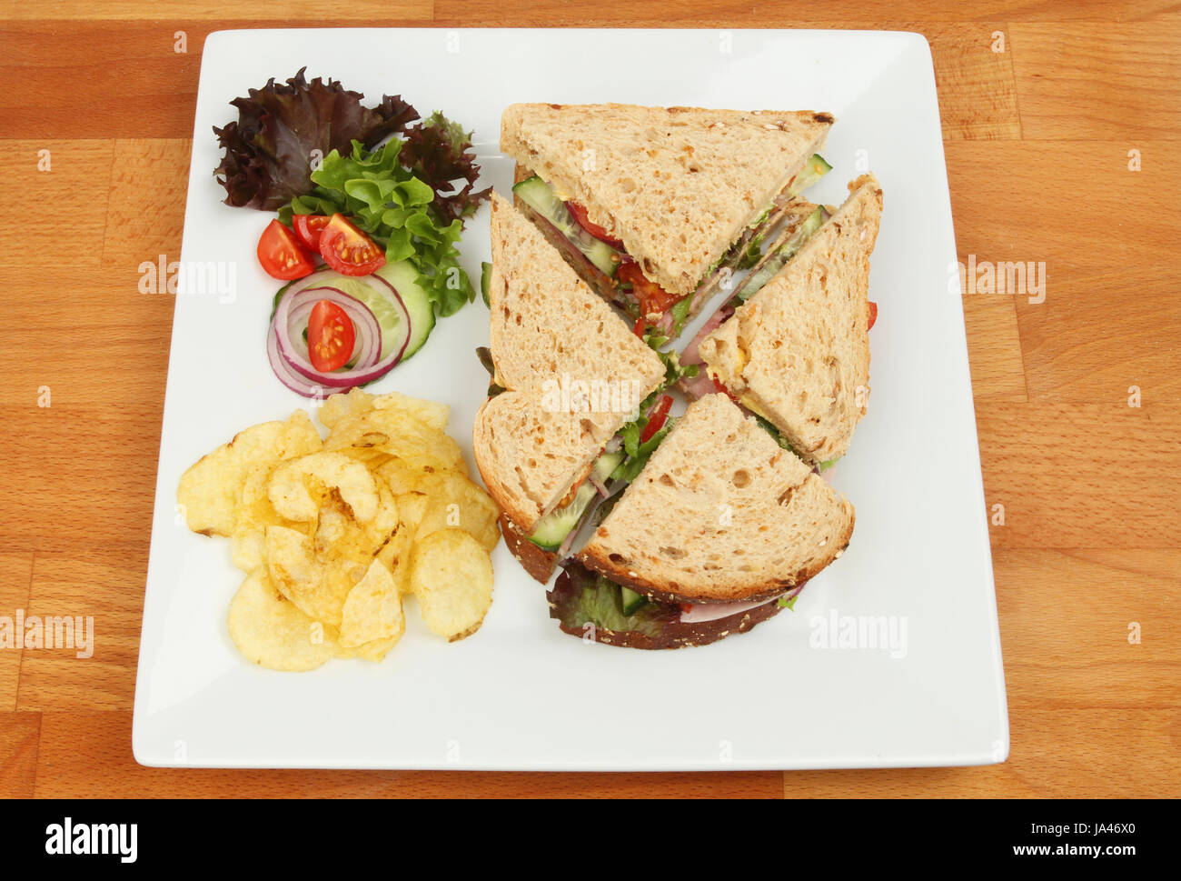 Ham salad sandwich with salad garnish and potato crisps on a plate on a wooden tabletop Stock Photo