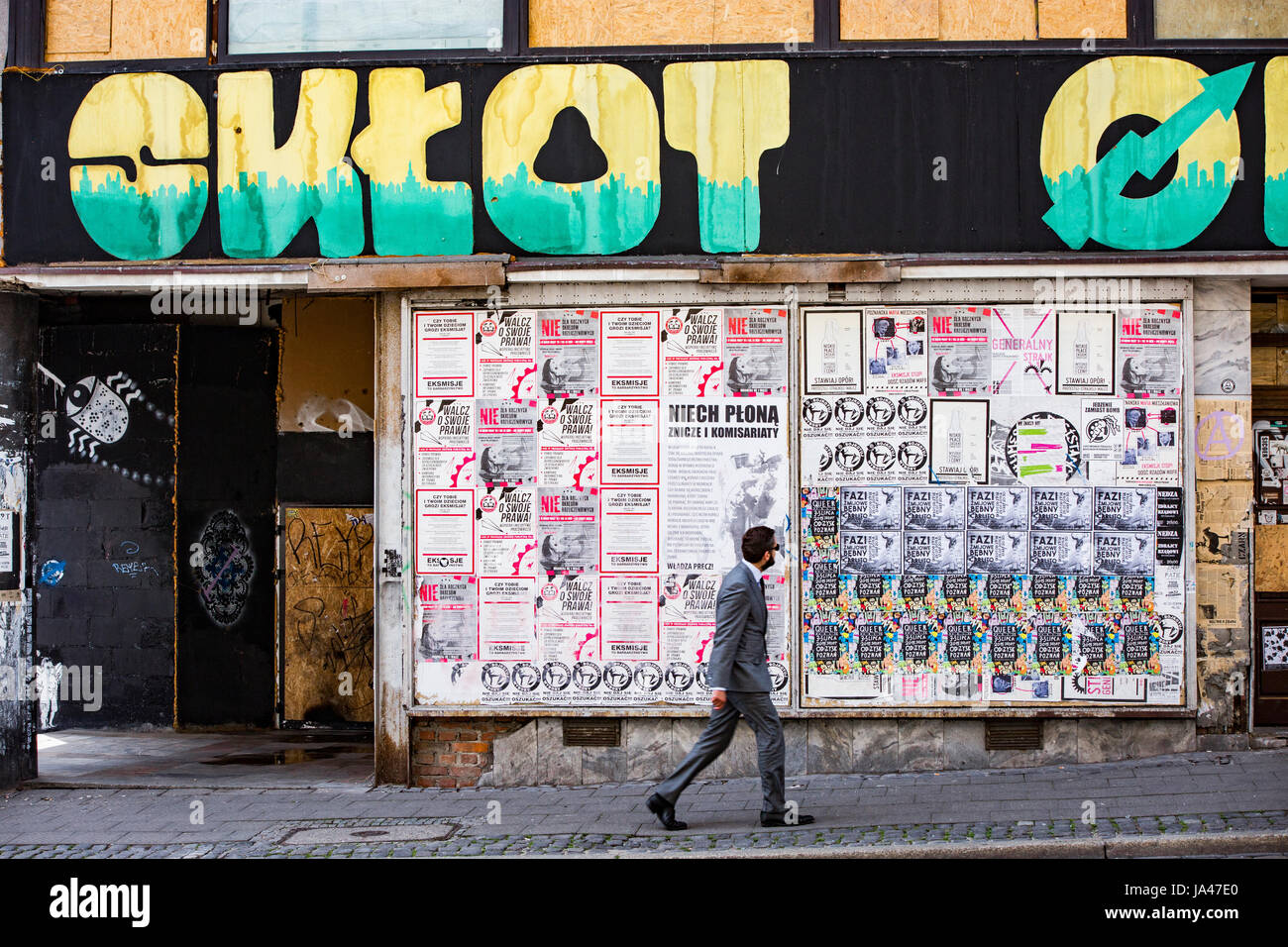 Yuppie man walking by squat, abandoned building occupying by squatters, watching or reading posters. Poznan, Poland. Stock Photo
