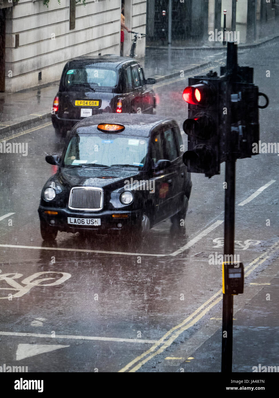 London Taxi in the rain. London Taxi Black Cab stops at traffic lights in a downpour. Stock Photo