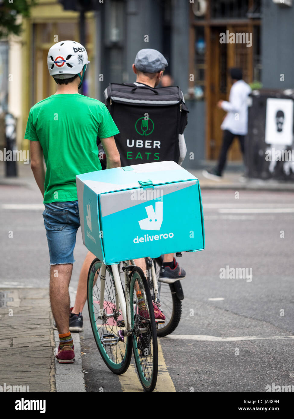 Deliveroo and Uber Eats food delivery bike couriers wait at traffic lights while delivering food to customers in Central London. Stock Photo