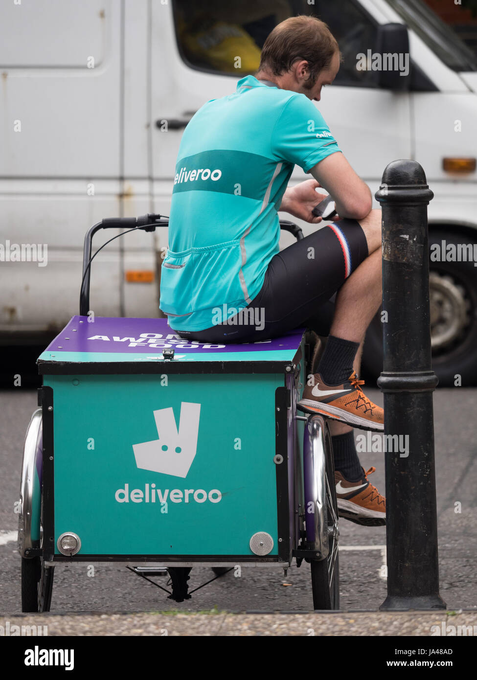 A Deliveroo cargo bike food delivery courier takes a break between