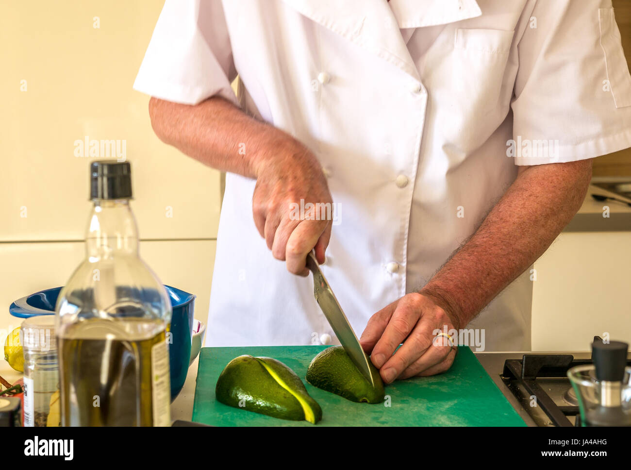 Older man in chefs whites slicing avocado on chopping board in kitchen, Scotland, UK Stock Photo