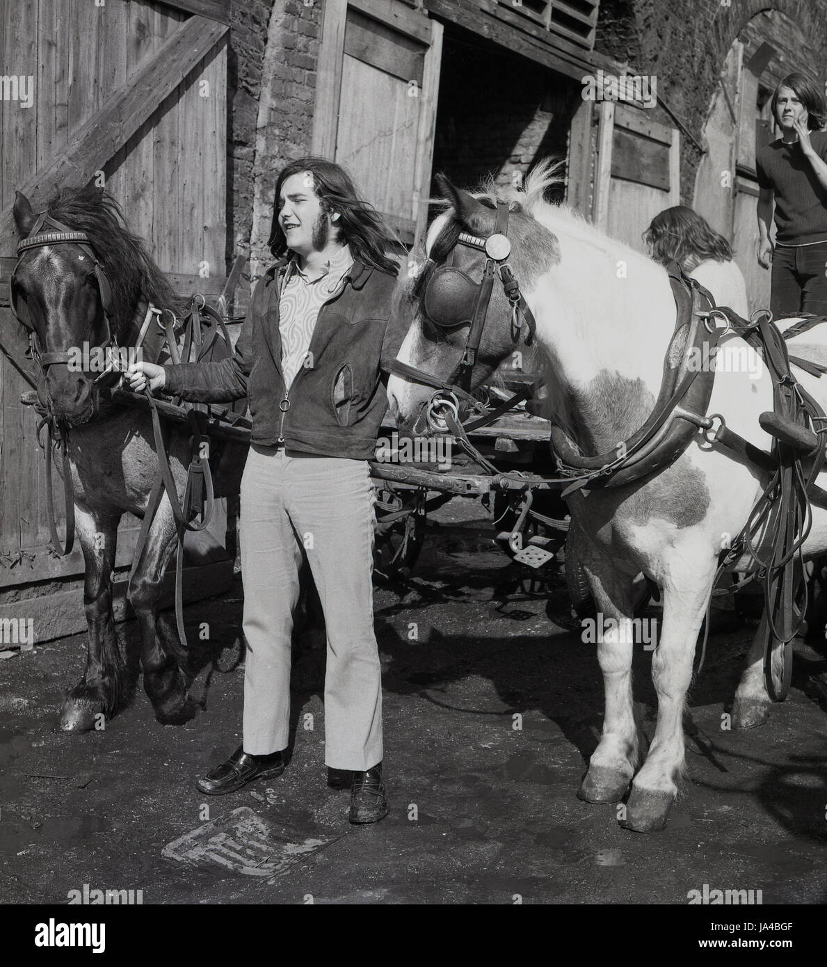 1971, historical, long haired male totter or rag-and-bone man holds the leather stirrups of his horses and carts outside railway arches, South London, Engand, UK. Stock Photo
