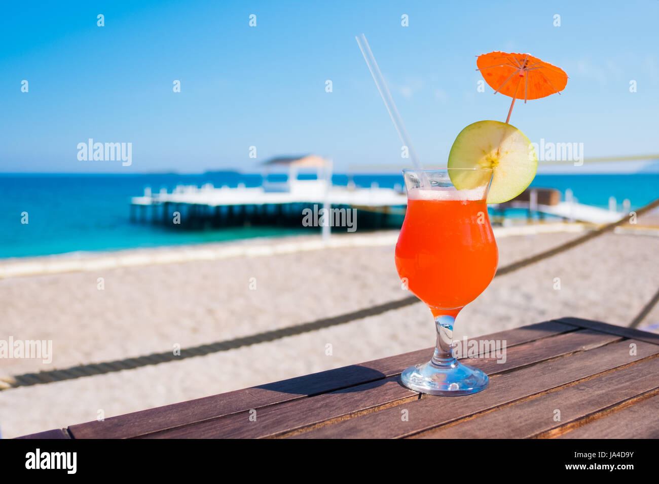 Orange cocktail with apple piece on wooden table. Sunny day near mediterranean sea. Summer time Stock Photo