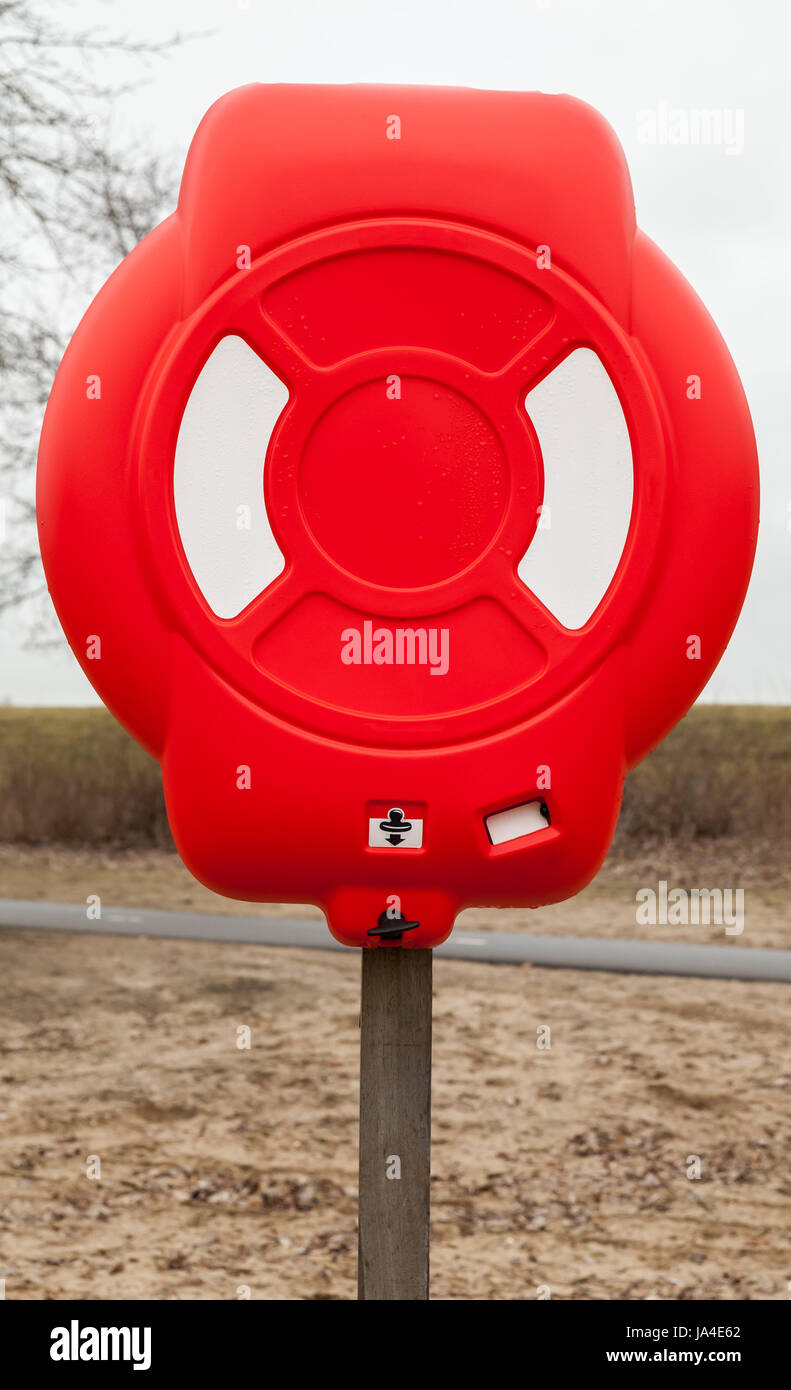 Bright red lifebuoy case on wooden pole stands on the beach Stock Photo