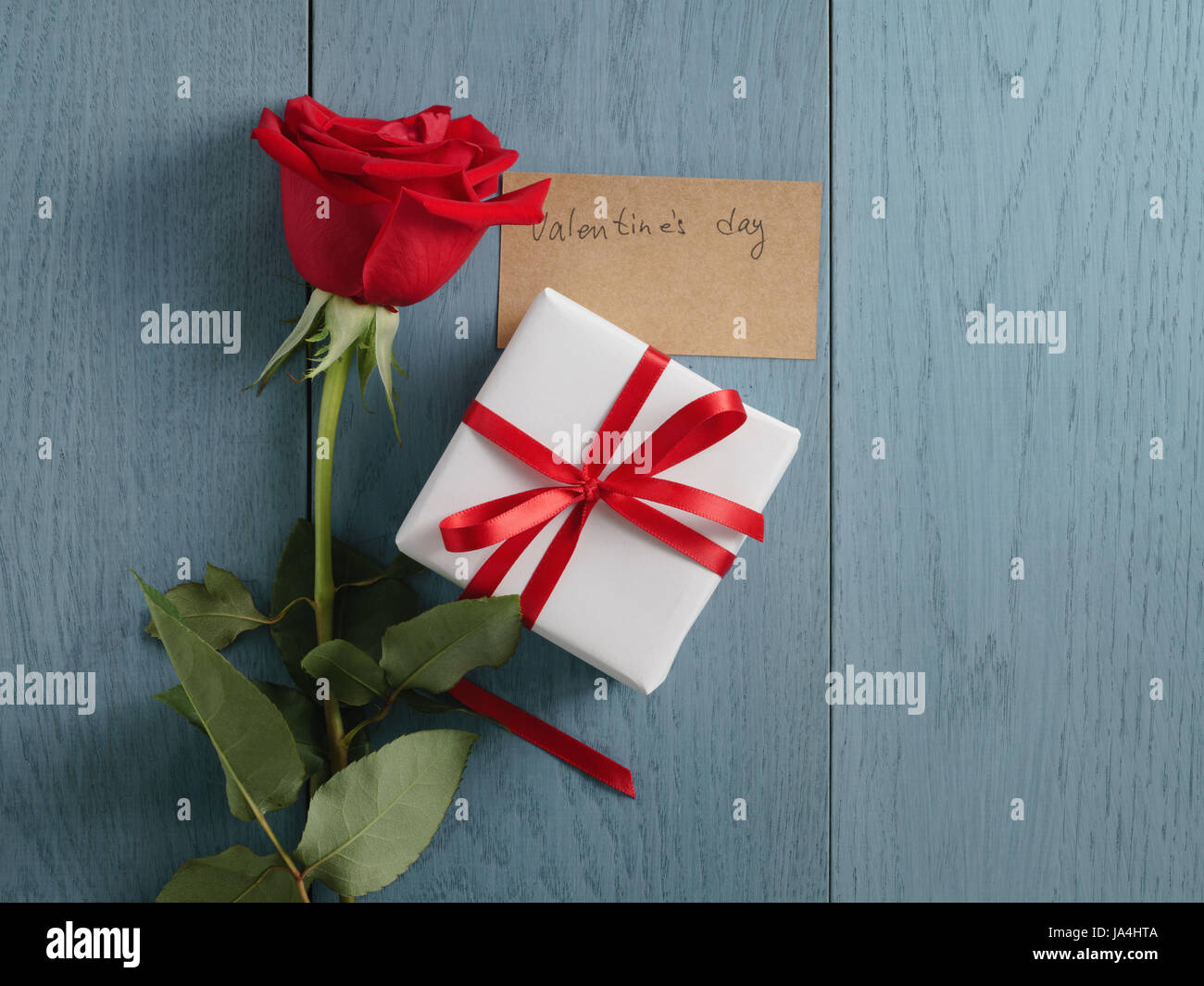 red rose with gift on blue wood table with valentines day paper card ...