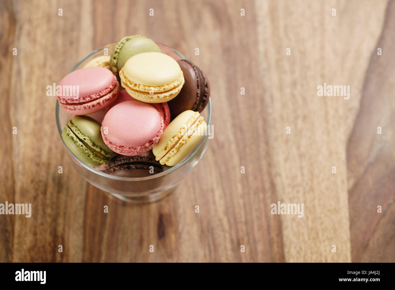 assorted macarons in glass bowl on wood table from above Stock Photo