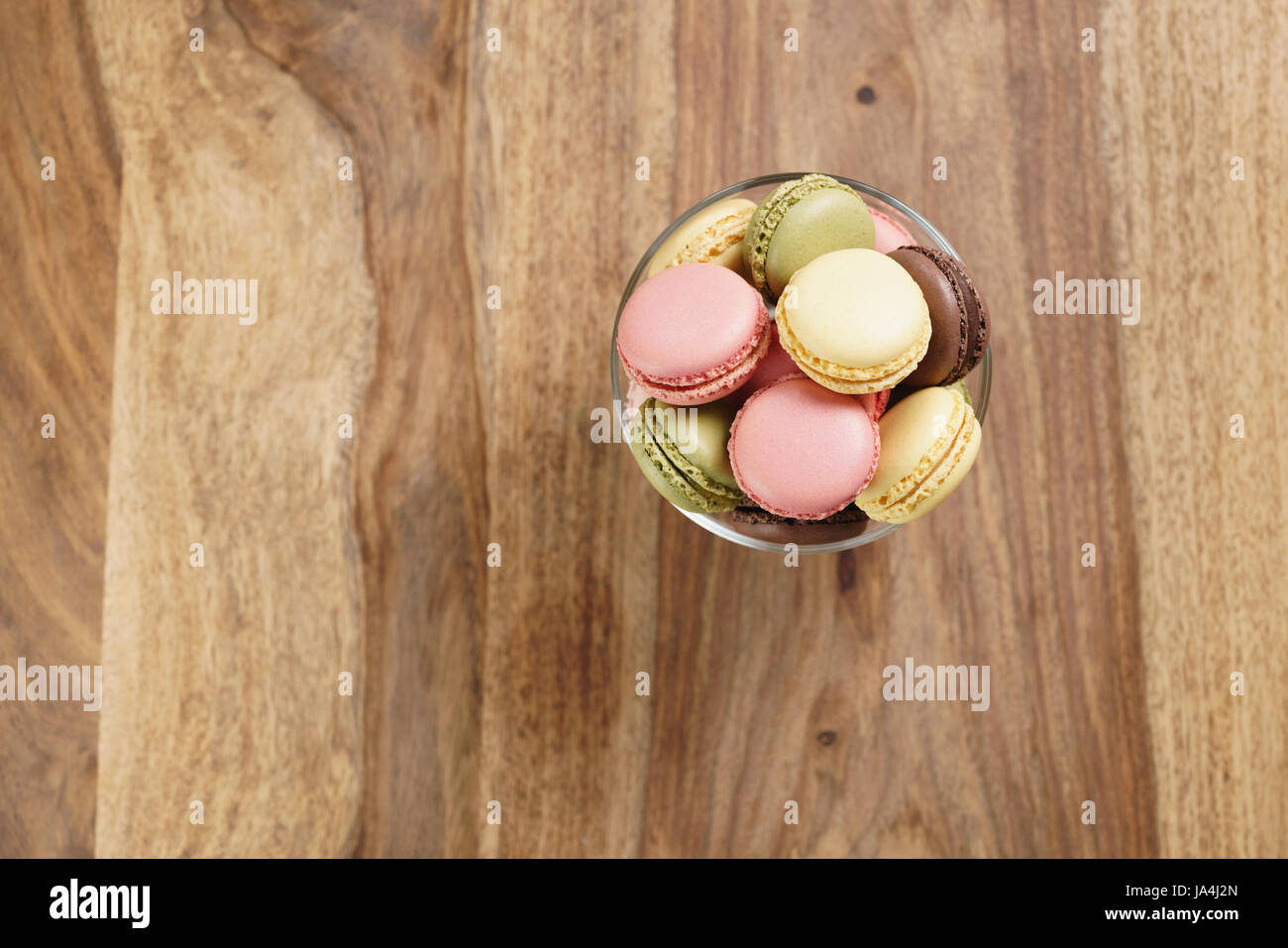 assorted macarons in glass bowl on wood table from above Stock Photo