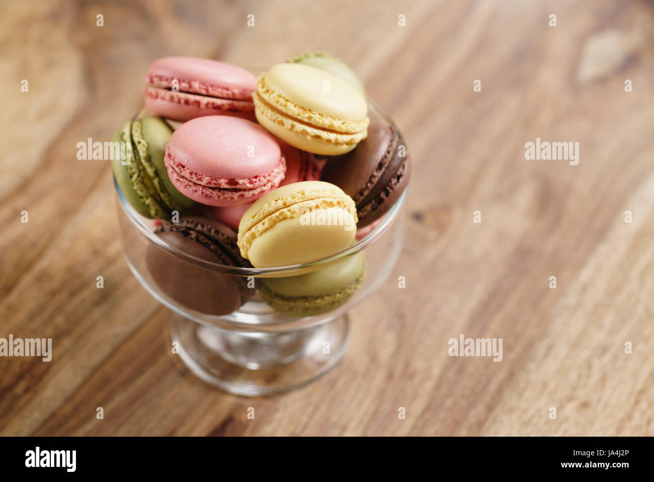assorted macarons in glass bowl on wood table from above Stock Photo