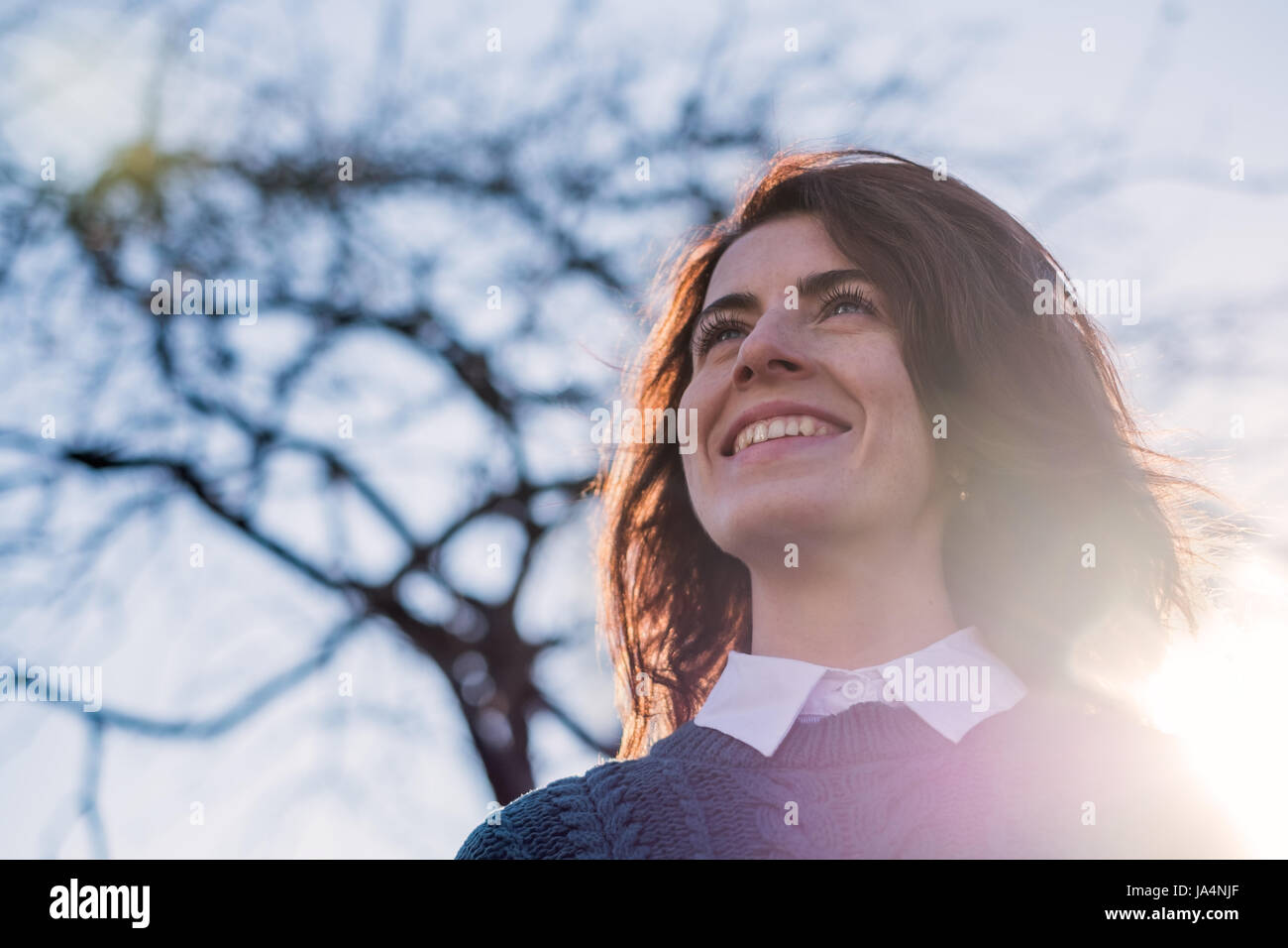 Red-haired girl smiles, enjoying the sun's rays. She crossed her arms behind her head. Positive mood for a walk Stock Photo