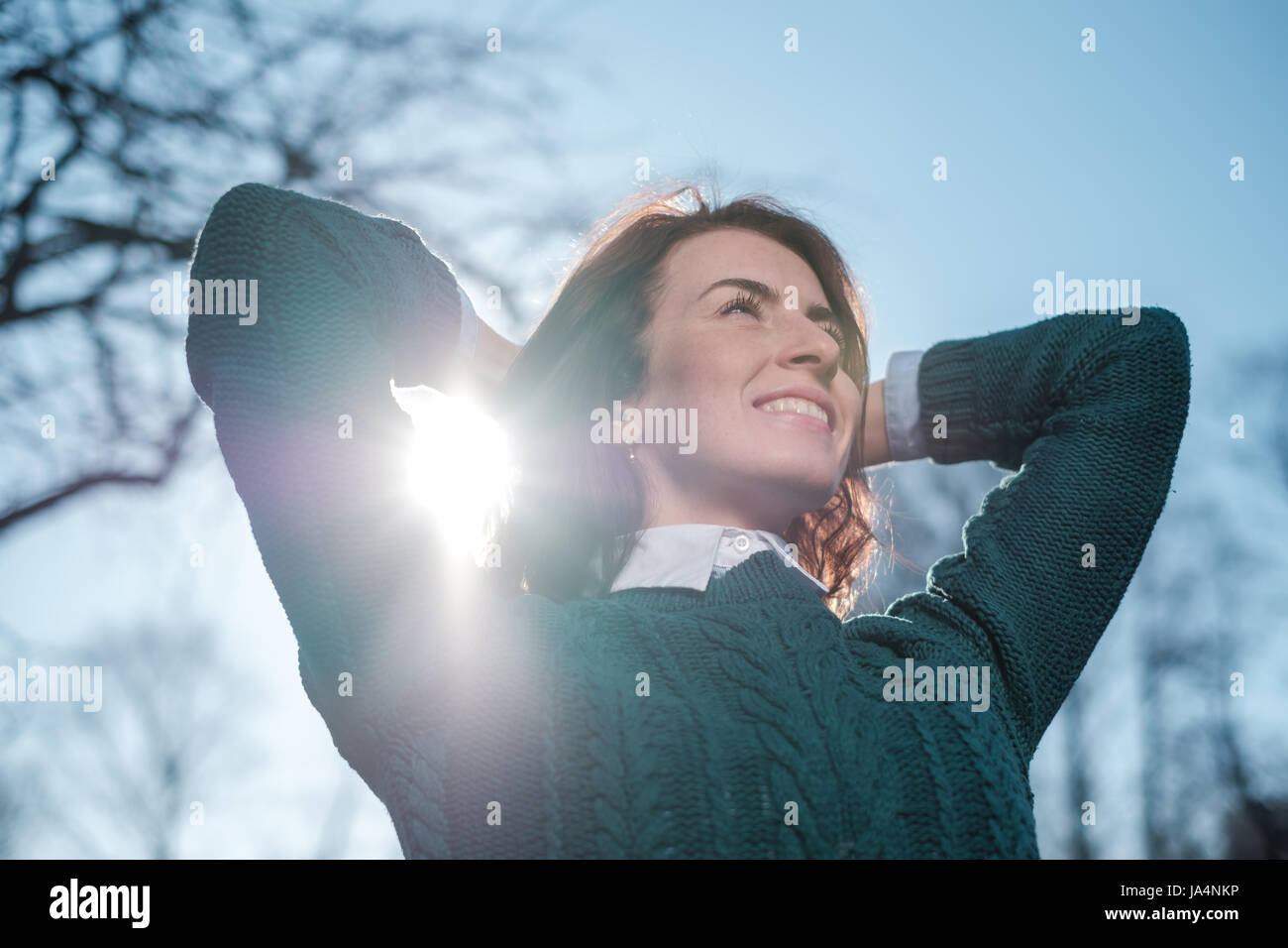Red-haired girl smiles, enjoying the sun's rays. She crossed her arms behind her head. Positive mood for a walk Stock Photo