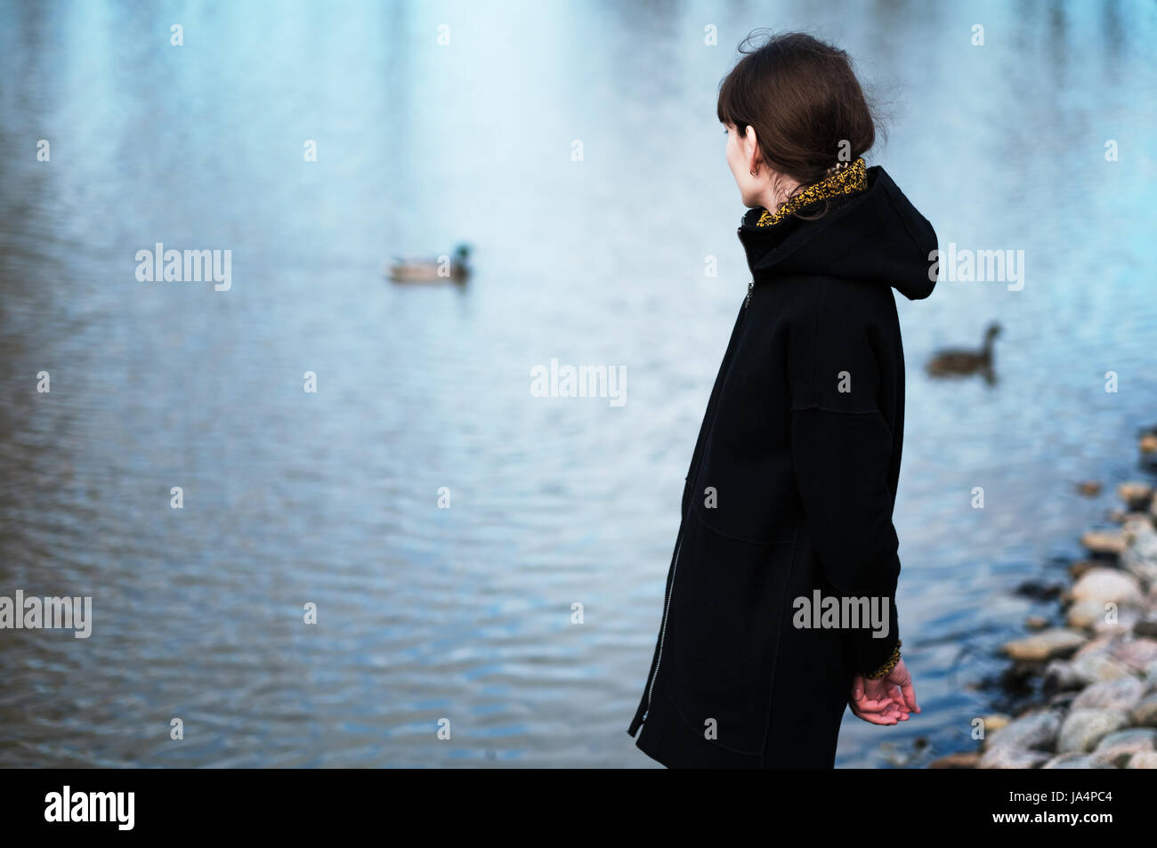 Portrait of a lonely girl by the lake. She stands in black clothes and looks sadly aside, I think about the sad thing Stock Photo