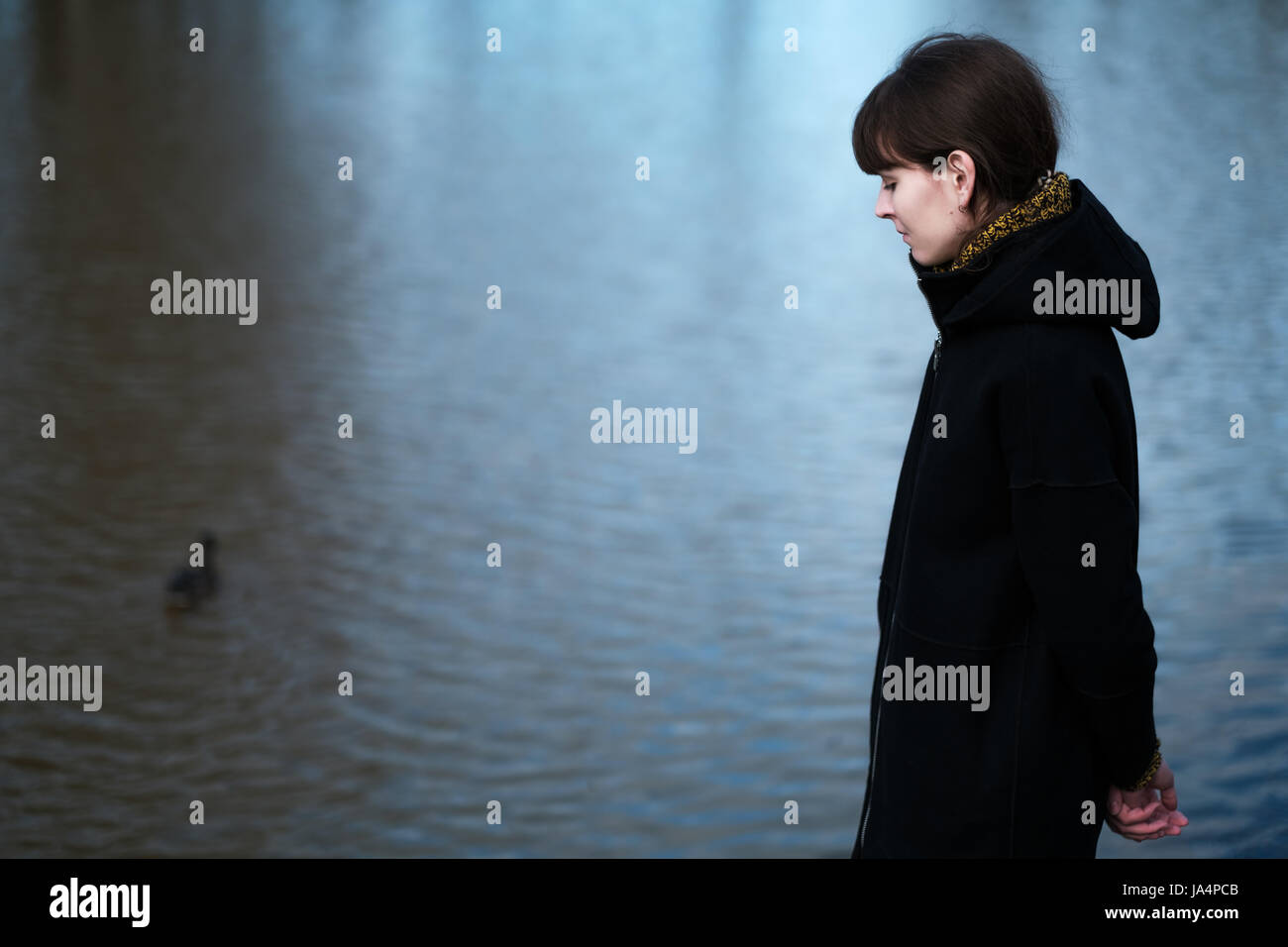 Portrait of a lonely girl by the lake. She stands in black clothes and looks sadly aside, I think about the sad thing Stock Photo