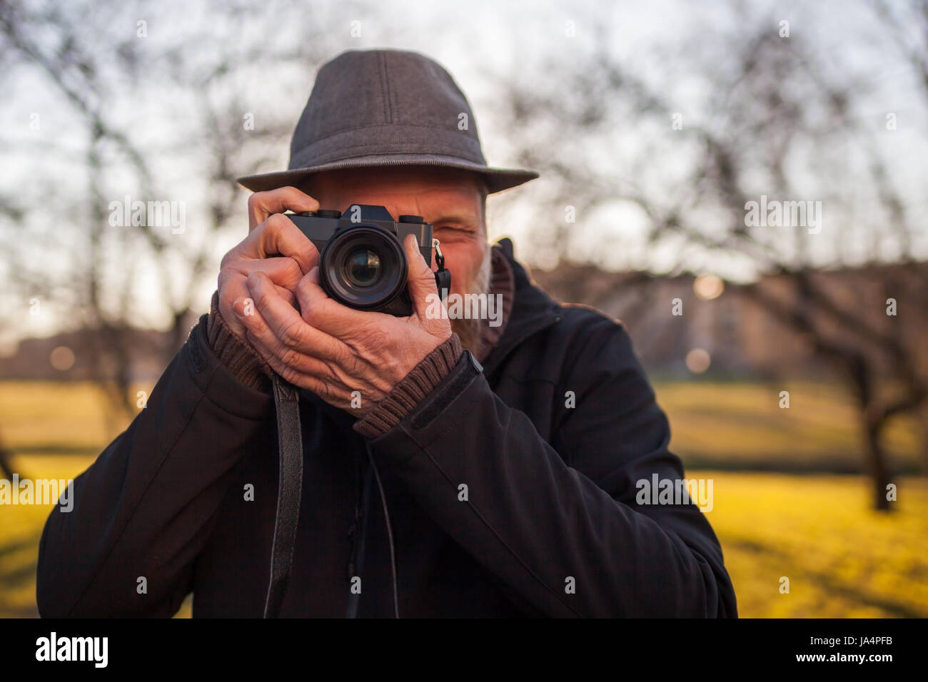 A mature man in a hat takes pictures on a mirrorless camera in the street. Hobby of photography. New trends in photographic technique. Stock Photo