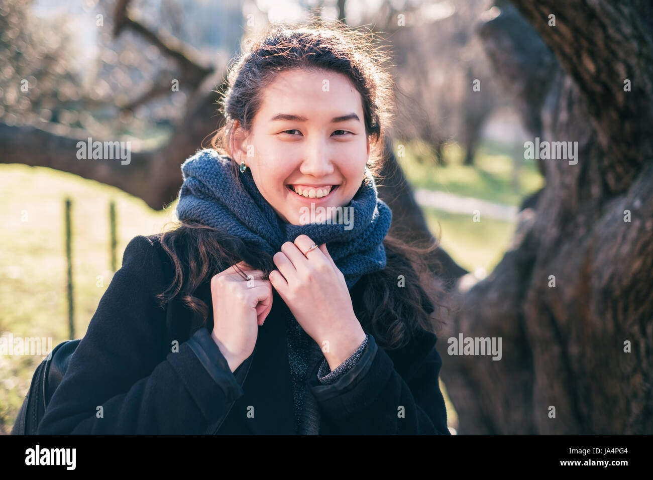 Portrait of an Asian happy girl. She looks at the camera and smiles, wrapped up in a scarf. Stock Photo