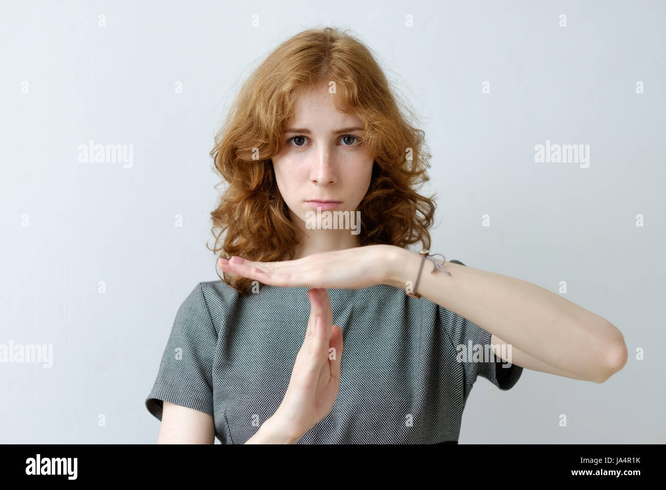 A red-haired girl with curly hair and freckles shows a sign of a timeout. Pause in work or relationship Stock Photo