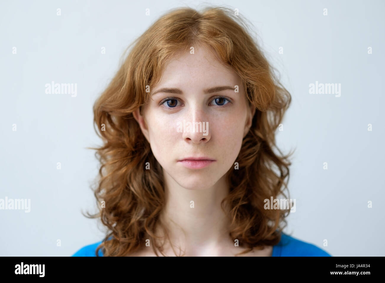 A red-haired girl with freckles looks ahead. Expression of a person without emotions. Stock Photo