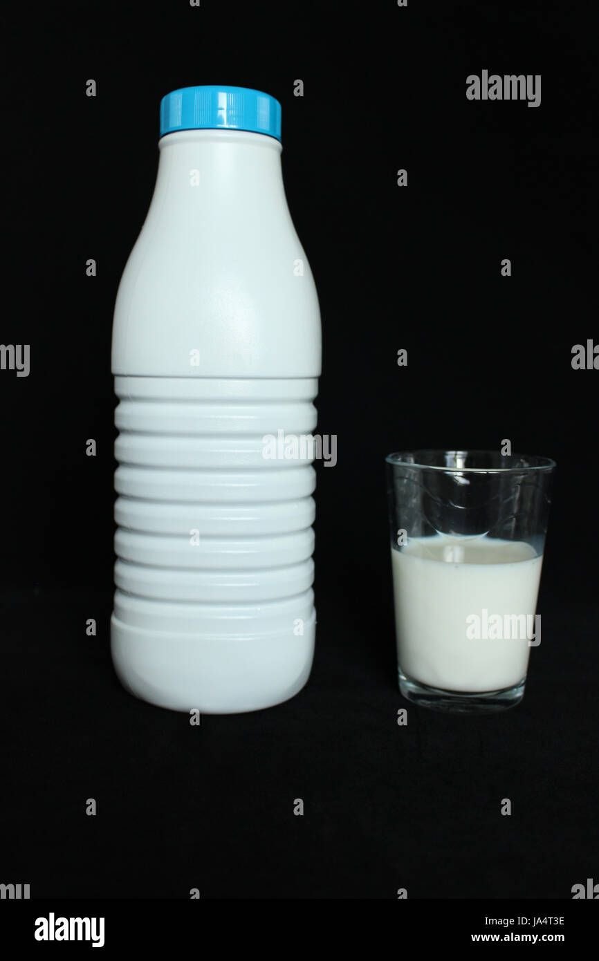 A bottle of milk with a glass filled with milk on a black background Stock Photo