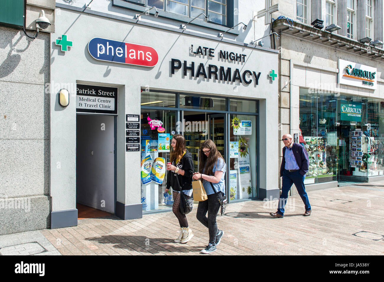 People walking past a late night pharmacy chemist on Patrick Street, Cork, Ireland. Stock Photo