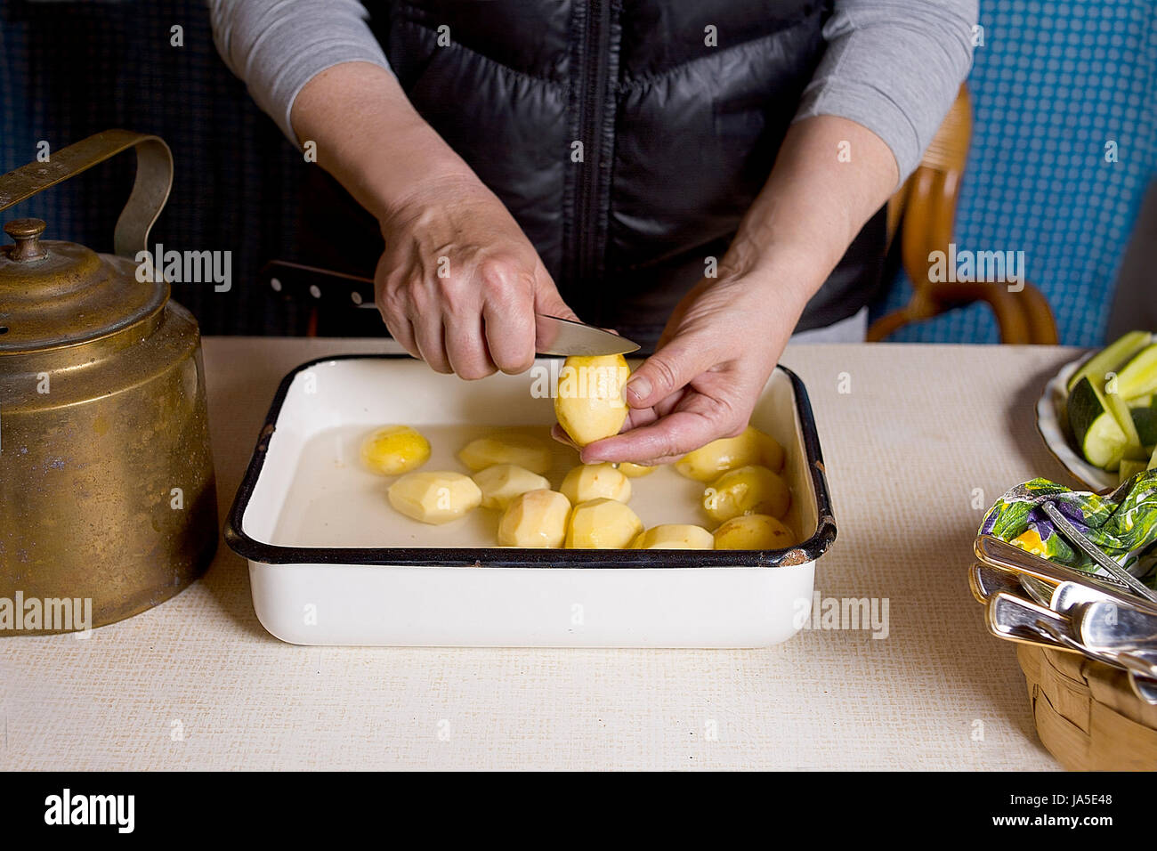 Female hands with kitchen knife peeling potato in a kitchen, interior