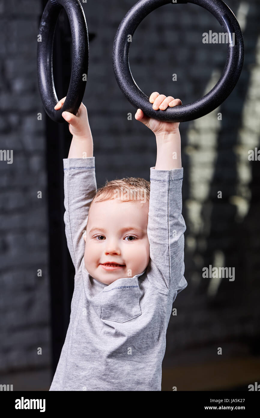 Cute child boy hanging on gymnastic rings in the cross fit gym against