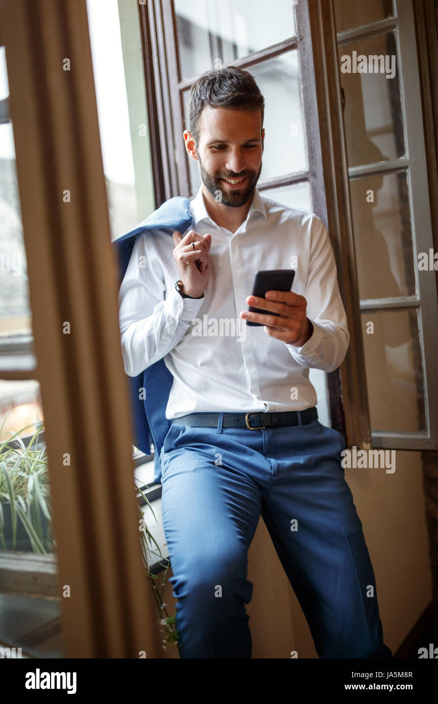 Male businessperson near window in office calling business partner on cell phone Stock Photo