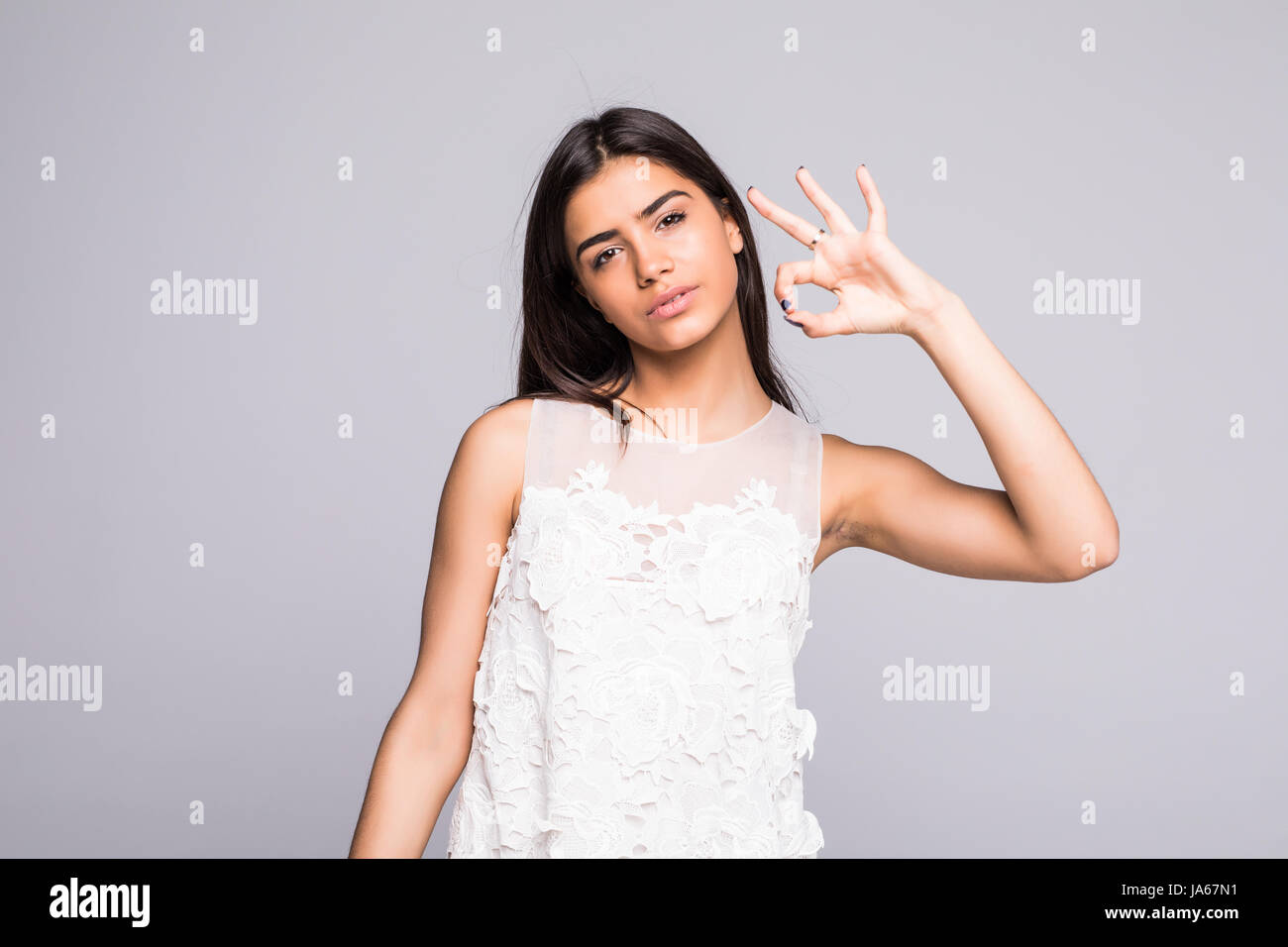 Young lighthearted girl shows Okay gesture, isolated on grey background Stock Photo