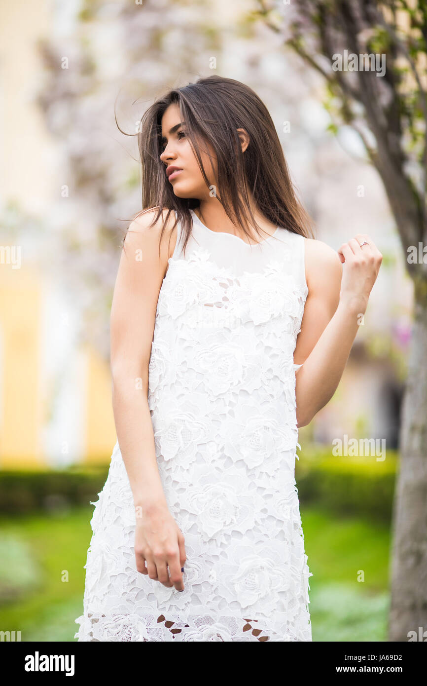 Beautiful attractive girl in dress posing in city park. Outdoor lifestyle fashion portrait of woman posing on the street Stock Photo