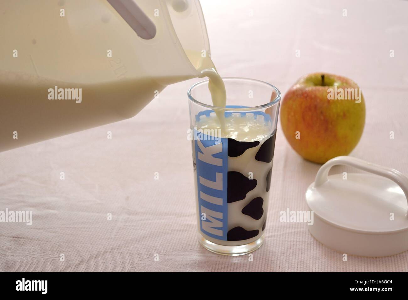 Jemand leert Milch in Glas, frischer Apfel liegt am Tisch Stock Photo