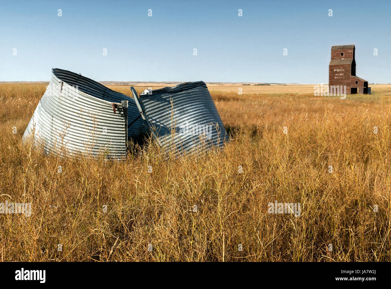 Abandoned grain elevator and scrap metal in prairie field. Stock Photo