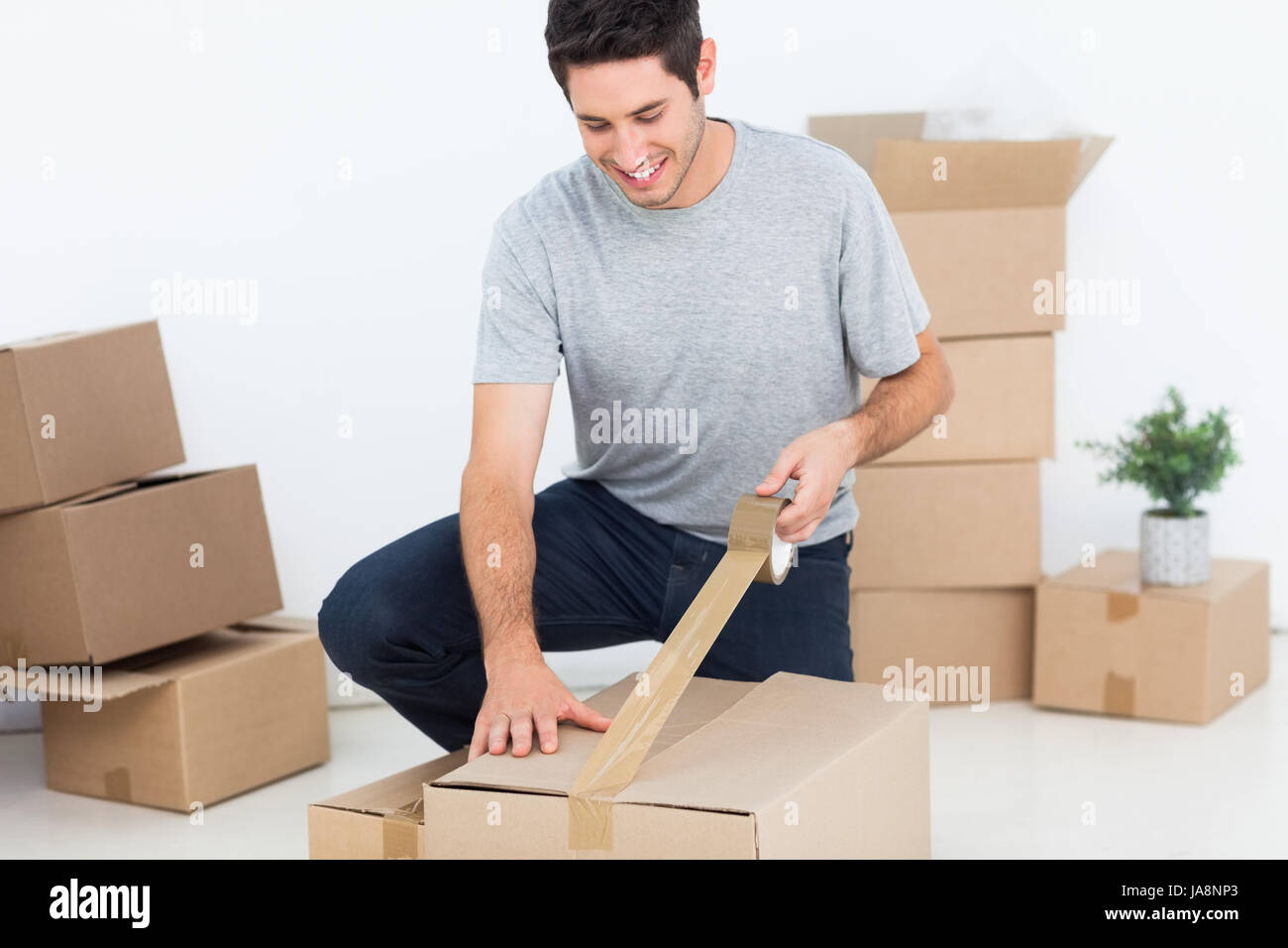 Happy man wrapping a box while he is moving home Stock Photo Alamy