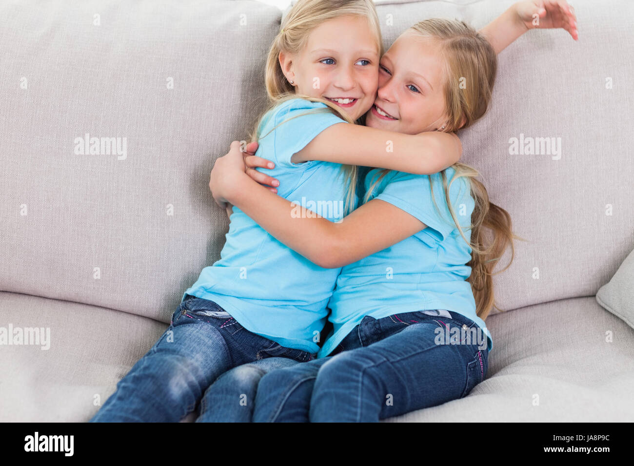 Young twins embracing each other sitting on a couch in the living room