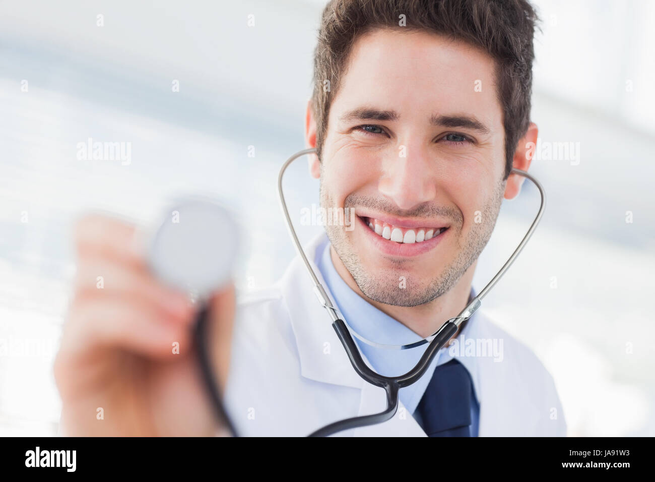 Smiling doctor with his stethoscope looking at camera in medical office ...