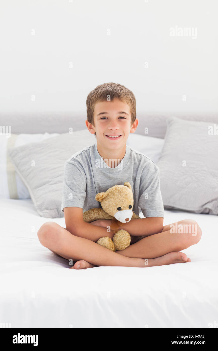 Little boy sitting on bed holding his teddy bear at home Stock Photo ...