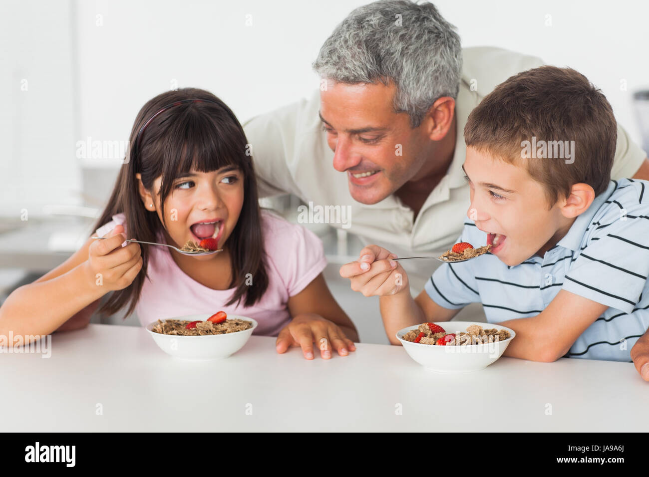 Smiling father talking with his children during their breakfast in kitchen Stock Photo