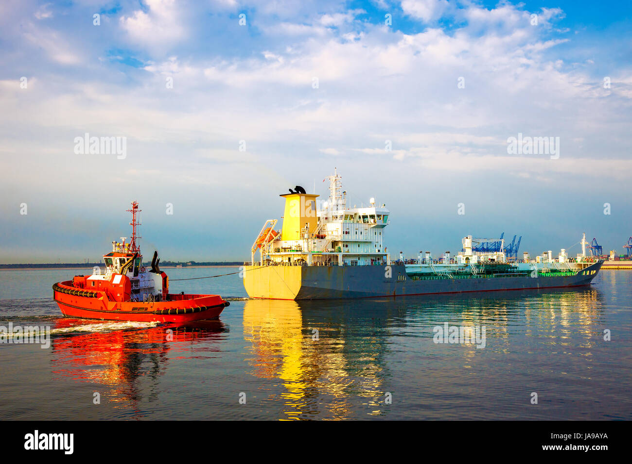 Tugboat towing tanker ship in port. Stock Photo