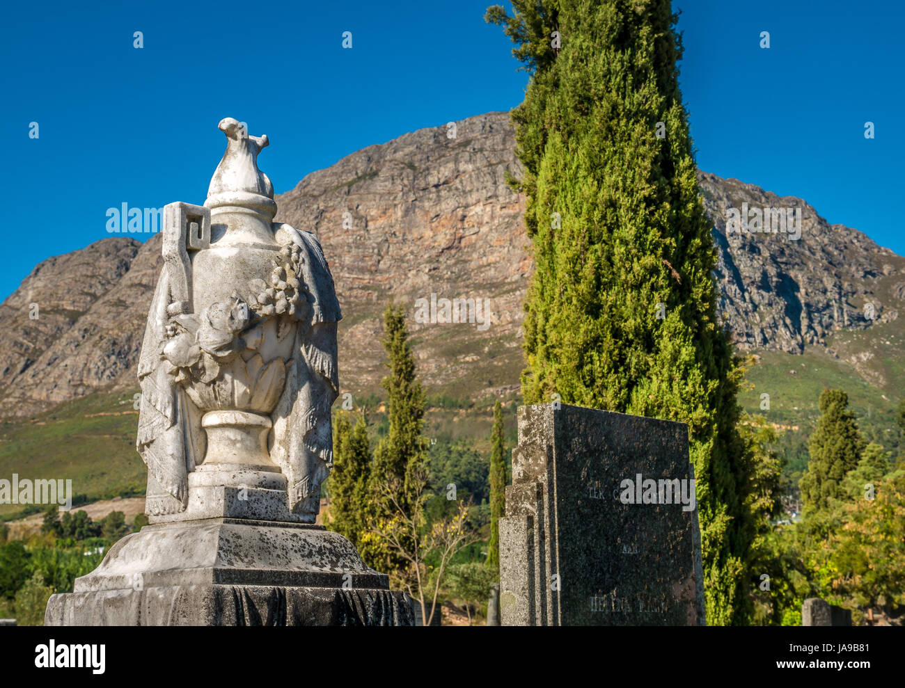 Symbolic draped urn gravestone memorial, French Huguenot cemetery, Franschhoek, Western Cape, South Africa, with mountain backdrop Stock Photo