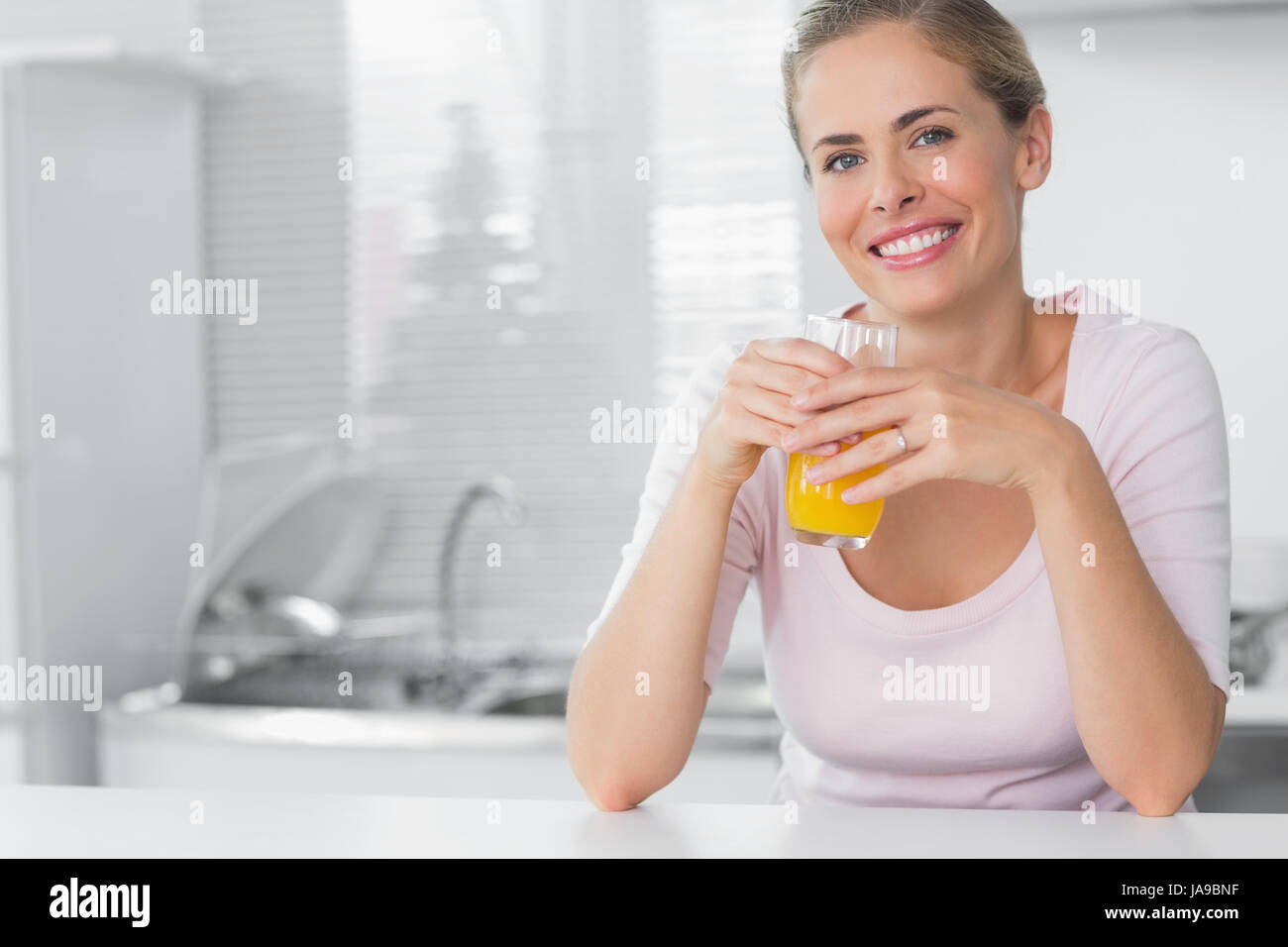 Cheerful blonde having orange juice in her kitchen Stock Photo Alamy