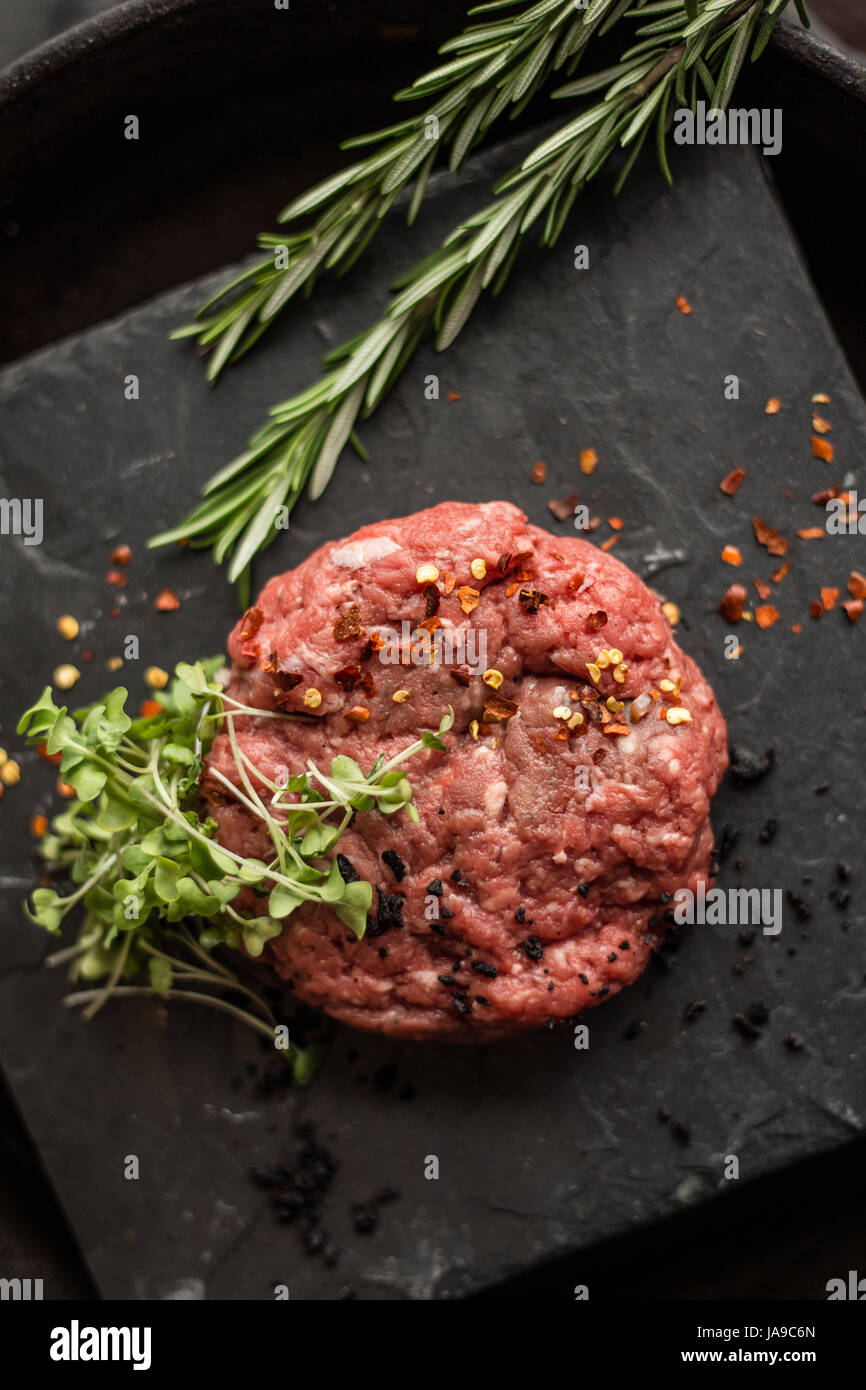 Raw ground beef meat steak cutlets with herbs and spices on black board. Restaurant Stock Photo
